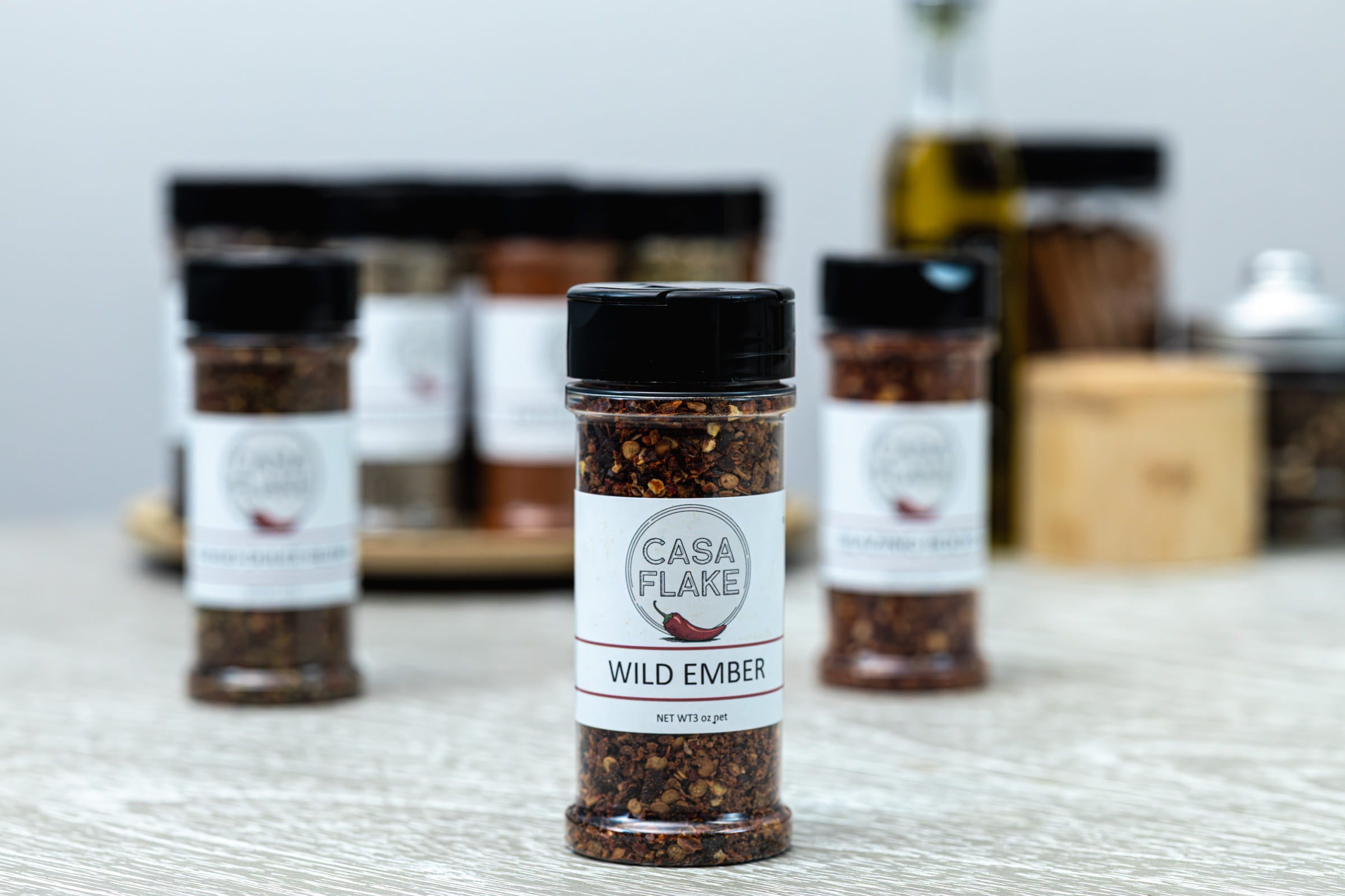 Casa Flake Wild Ember seasoning bottle on a wooden surface with other seasoning bottles in the background.