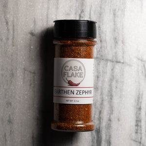 A clear plastic spice jar of Casa Flake Earthen Zephyr seasoning with a black lid and white label, set against a gray marble background.