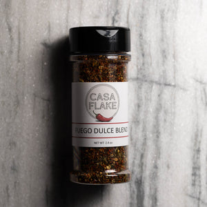 A clear plastic spice jar of Casa Flake Fuego Dulce Blend with a black lid and white label, set against a gray marble background.