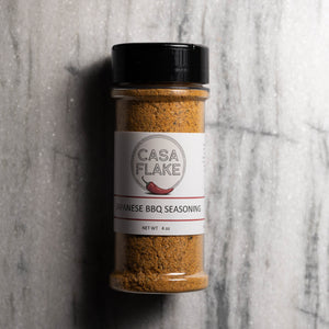 A 4 oz clear plastic spice jar of Casa Flake Japanese BBQ Seasoning with a black lid and white label, set against a gray marble background.