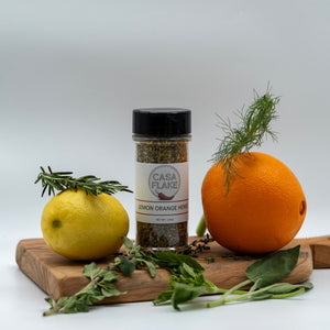 Casa Flake Lemon Orange Herb seasoning bottle on a wooden board with lemon, orange, and herbs.
