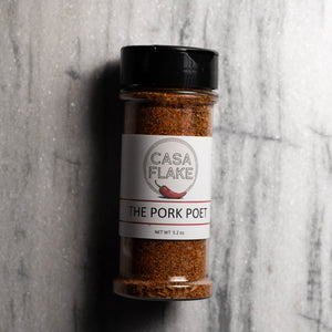 A 5.2 oz clear plastic spice jar of Casa Flake 'The Pork Poet' seasoning, featuring a white label and a black shaker lid, set against a gray marble background.