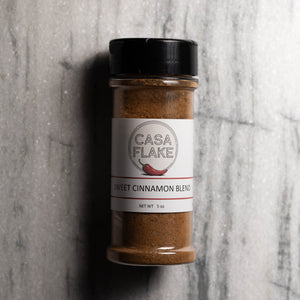 A 5 oz clear plastic spice jar of Casa Flake Sweet Cinnamon Blend with a black lid and white label, set against a gray marble background.