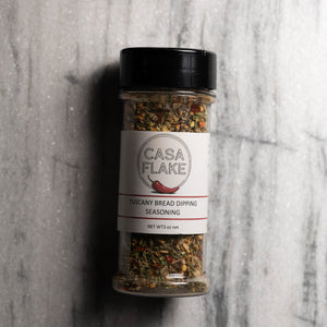 A clear plastic bottle of Casa Flake Tuscany Bread Dipping Seasoning with a black lid and white label, set against a gray marble background.